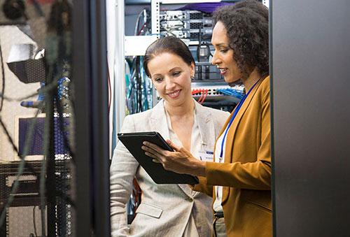 2 women viewing tablet in computer server room