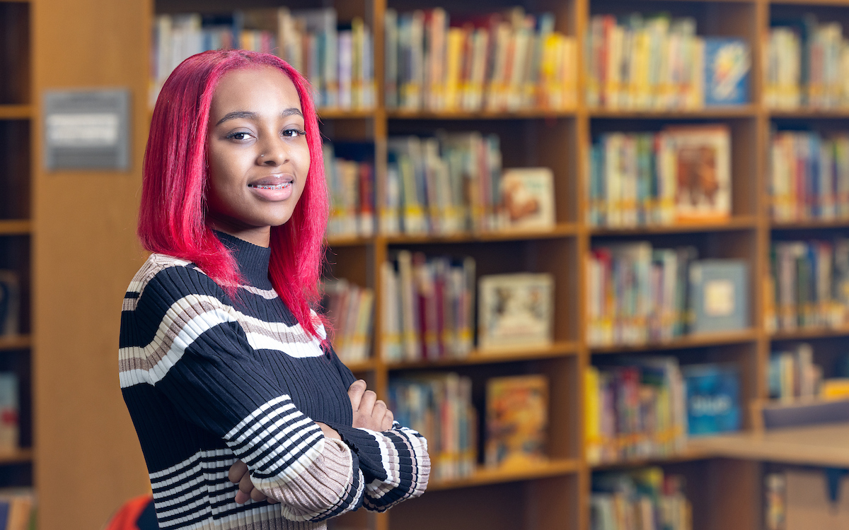 Image of student, Skye Stonestreet, posing in front of library bookshelves.