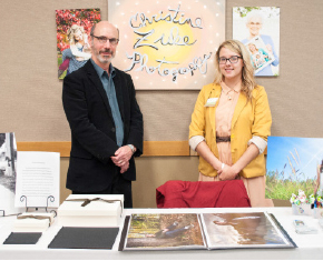 Photography faculty Terry Abrams stands with graduating student Chrissy Zuke at her booth.