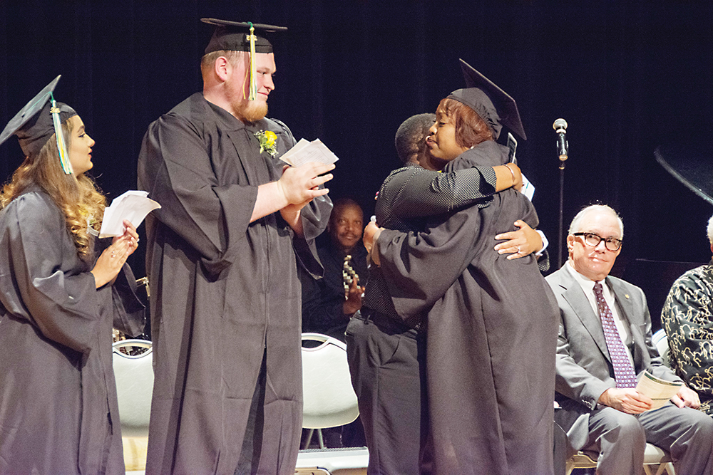 An emotional Dorothy Jett (far right) hugs the other speakers on the podium following her speach during an Adult Transitions GED Plus program graduation ceremony. “I’m 53, but I finally did it,” Jett told those in attendance. | Photo by CJ South
