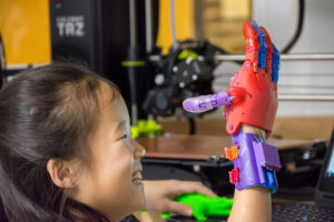 Lucy checks out her prosthetic near the WCC 3-D printers that created the hand. | Photo by CJ South