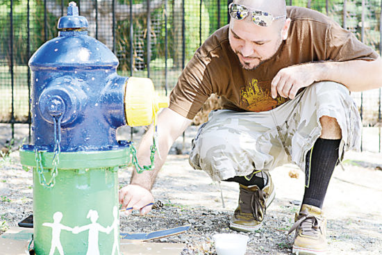 WCC student Damien Lamberti paints a worn fire hydrant at the Lake Shore Apartments in Ypsilanti Township. (Photo by CJ South)