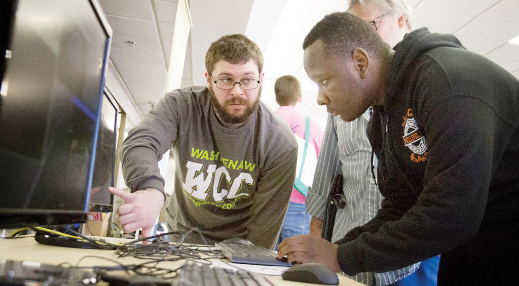 Caleb Stade (center) helps Belleville High School student Derrick Loutharp enter code into a mock system meant to demonstrate car programming during Free College Day on April 7. (Photo by Kelly Gampel)