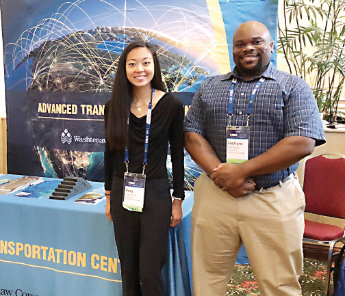 Washtenaw Community College students Rosa Lechartier and Zachyre Van Buren stand at the college’s exhibit during the Center for Automotive Research Management Briefing Seminars in Traverse City.