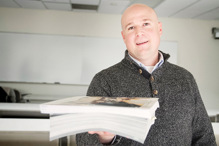 WCC Business instructor Douglas Waters holding an expensive textbook he replaced with a free online alternative