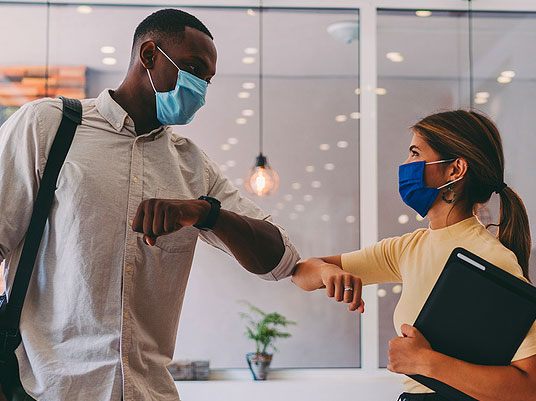 two masked people giving an elbow bump